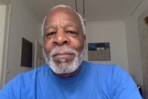 Ronald Bunn wearing a blue T shirt with an African painting hanging over his left shoulder